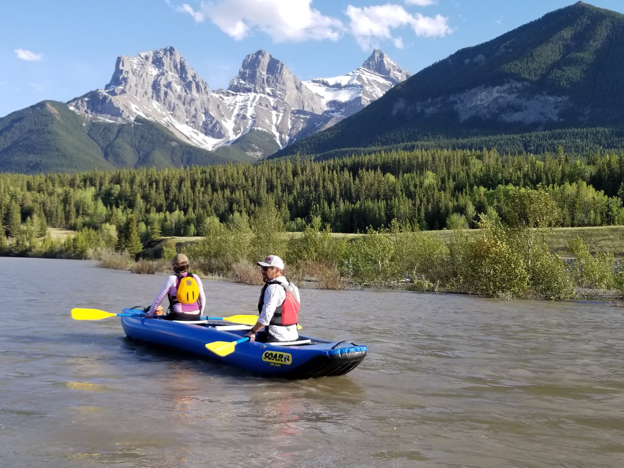 Two people canoe on a river near the Three Sisters mountains in Canmore