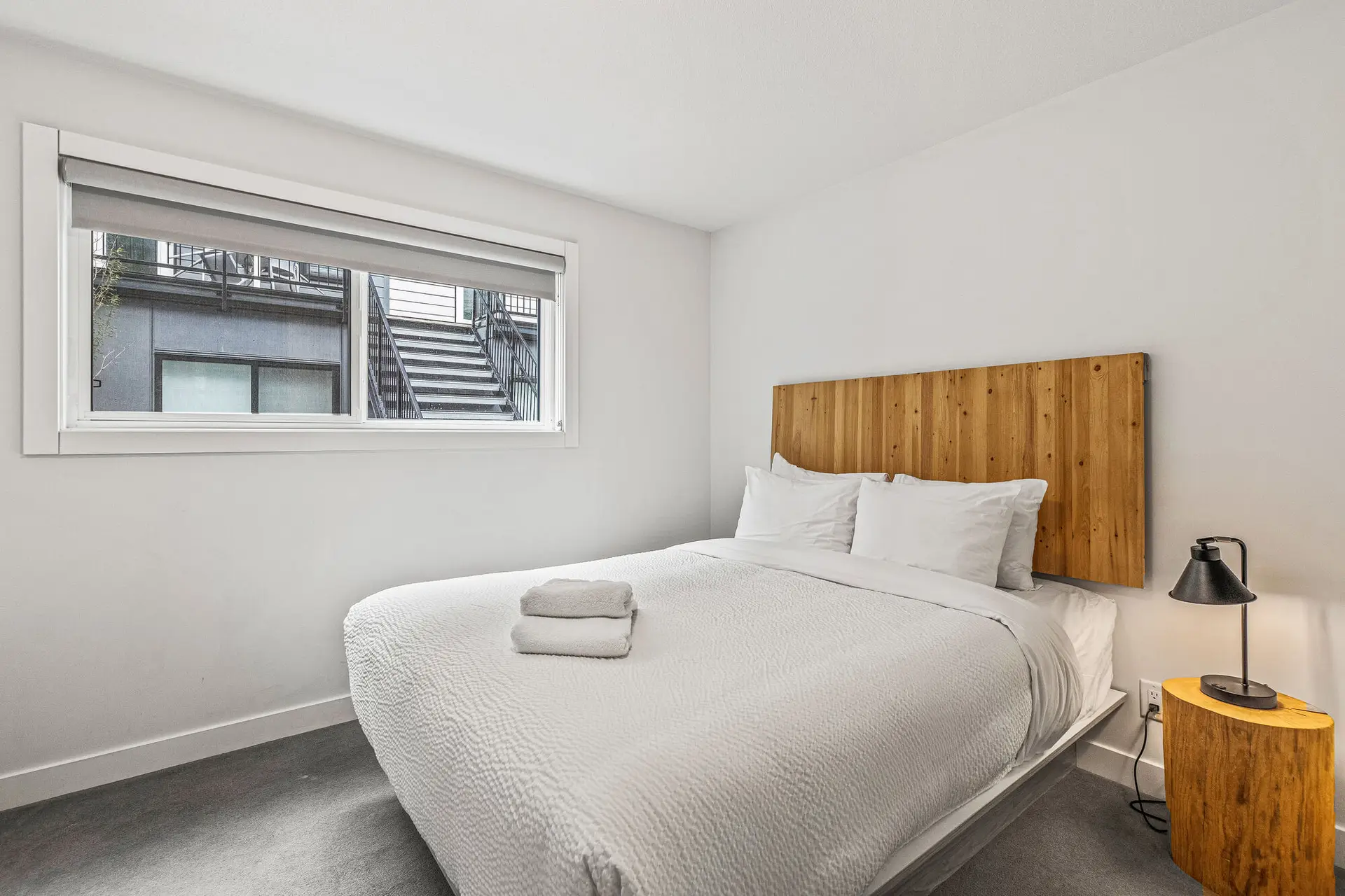 Queen bed in a modern Canmore resort suite with wooden headboard and bedside lamp.