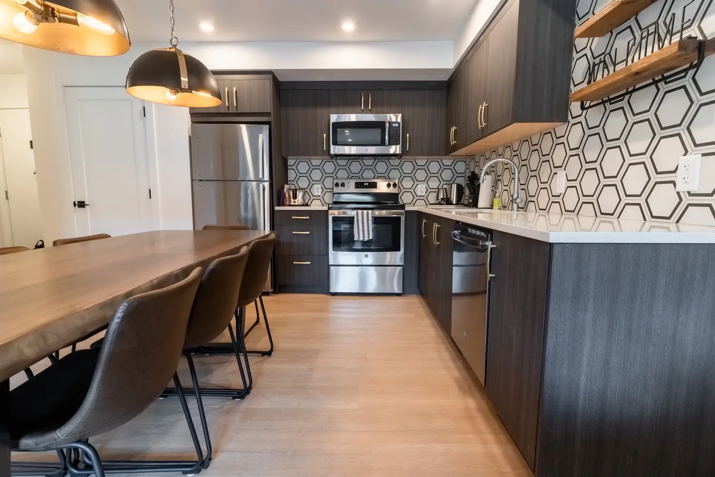Modern kitchen with dark cabinets, stainless steel appliances, and a dining table at Basecamp Suites Canmore.