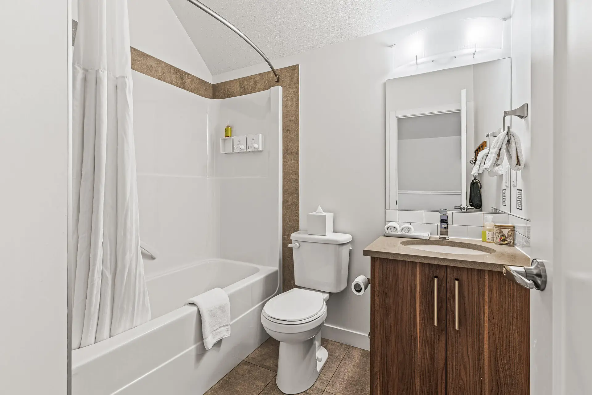 Modern bathroom with white bathtub, toilet, and vanity in a Basecamp Resorts Canmore suite.