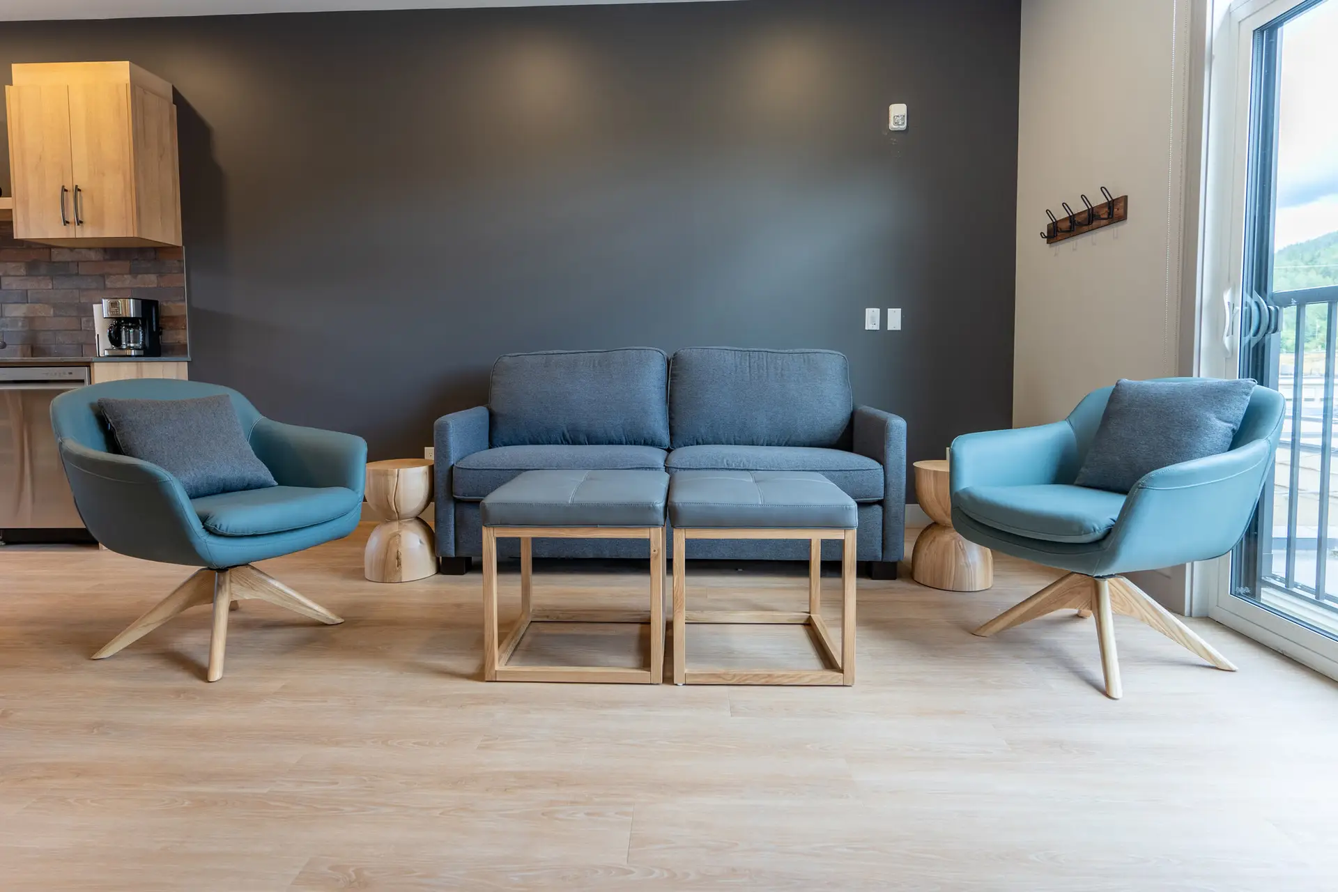 Basecamp Suites Revelstoke: Blue armchairs, sofa, and ottomans in a modern living area.