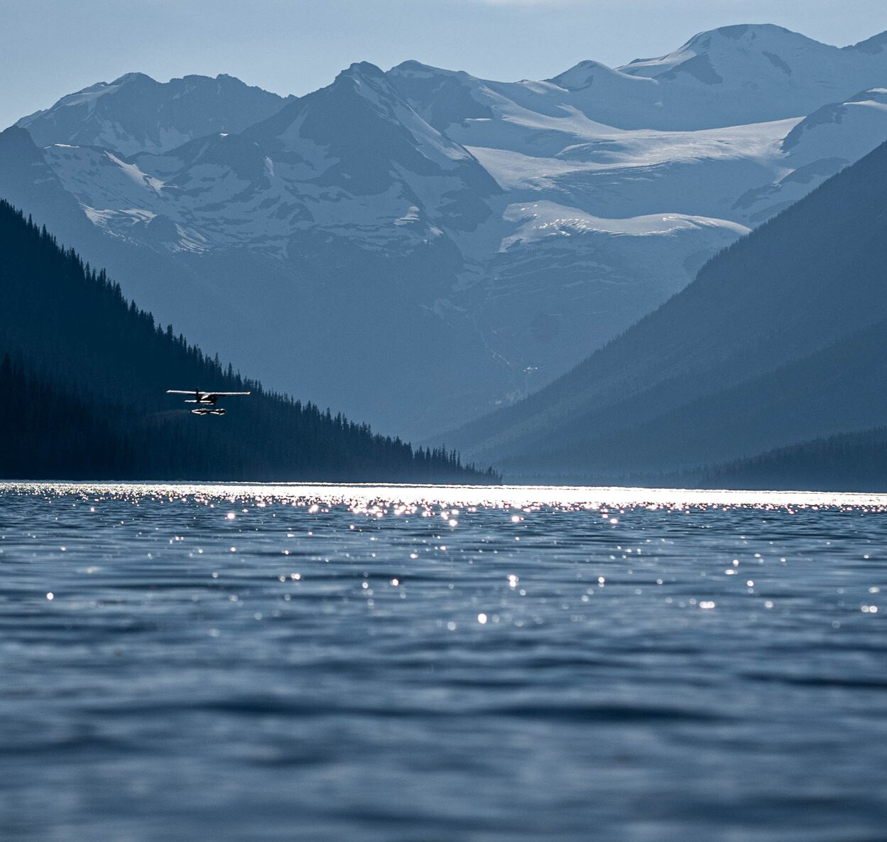 Silvertip Aviation floatplane flying over a sparkling lake with mountains.