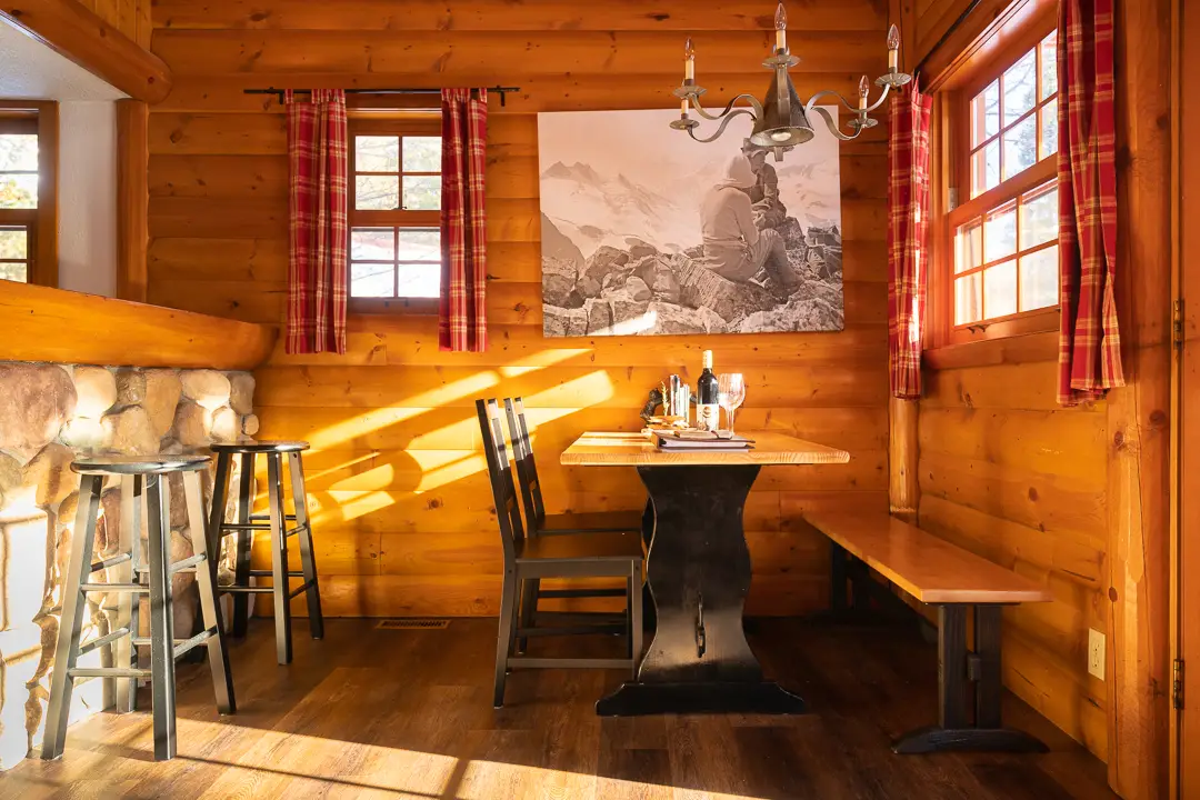 Rustic dining area in Basecamp Baker Creek cabin with wood walls and checkered curtains.
