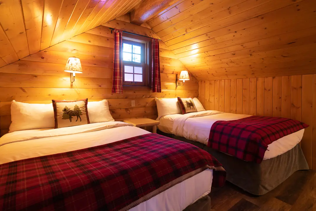 Loft bedroom in Basecamp Baker Creek cabin with two beds and plaid blankets.