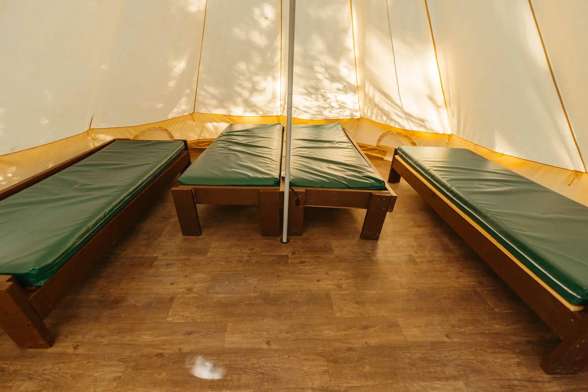 Interior of a canvas bell tent with three wooden cots with green mattresses