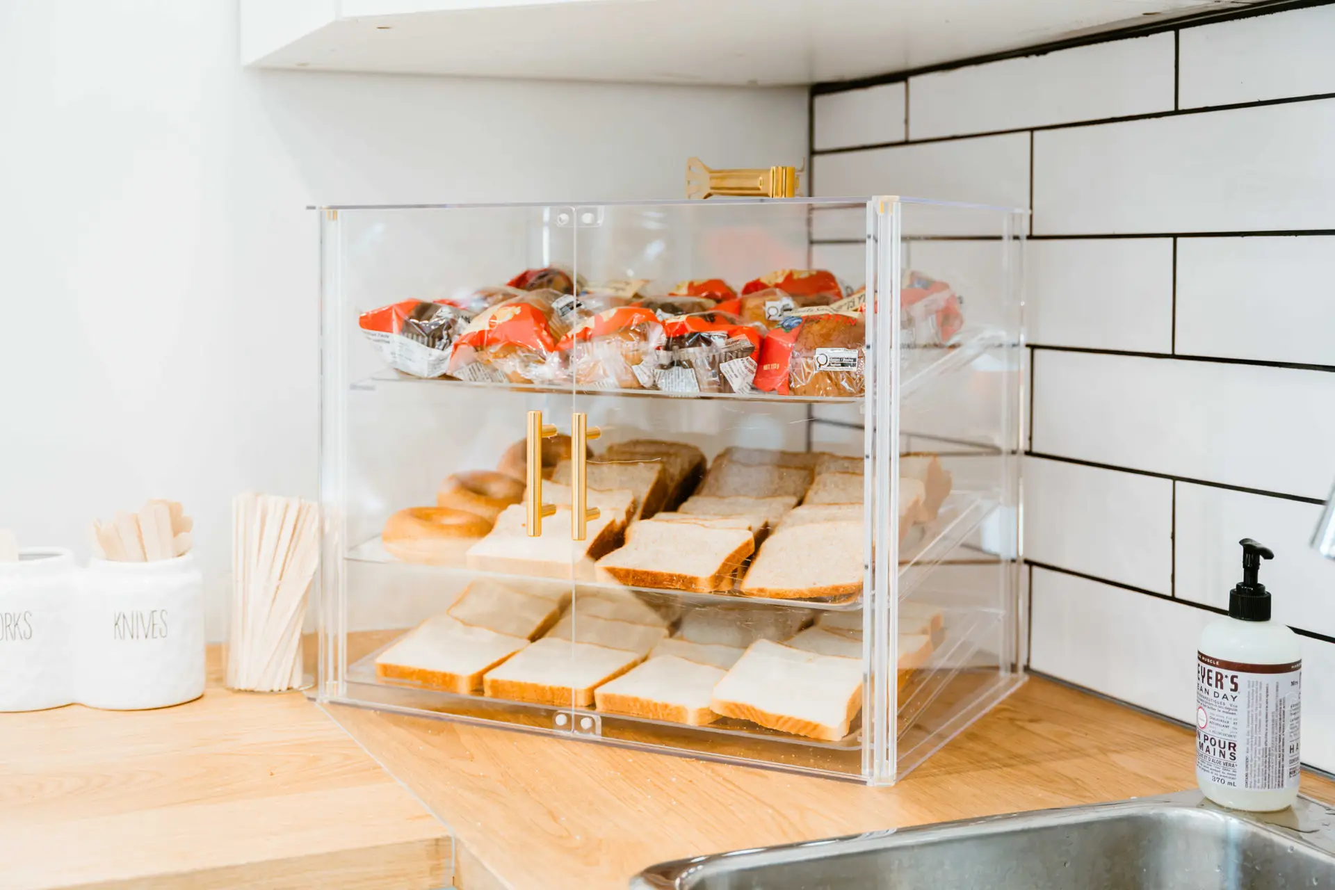Continental breakfast display with pastries, bagels, and sliced bread in a clear case.