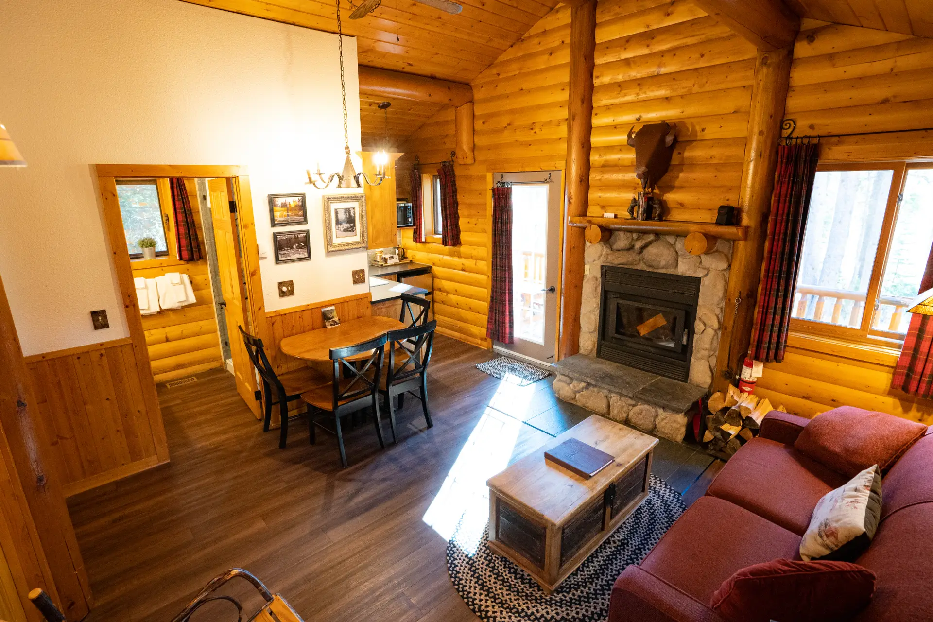 Interior of a cozy log cabin living room with fireplace, dining table, and sofa.