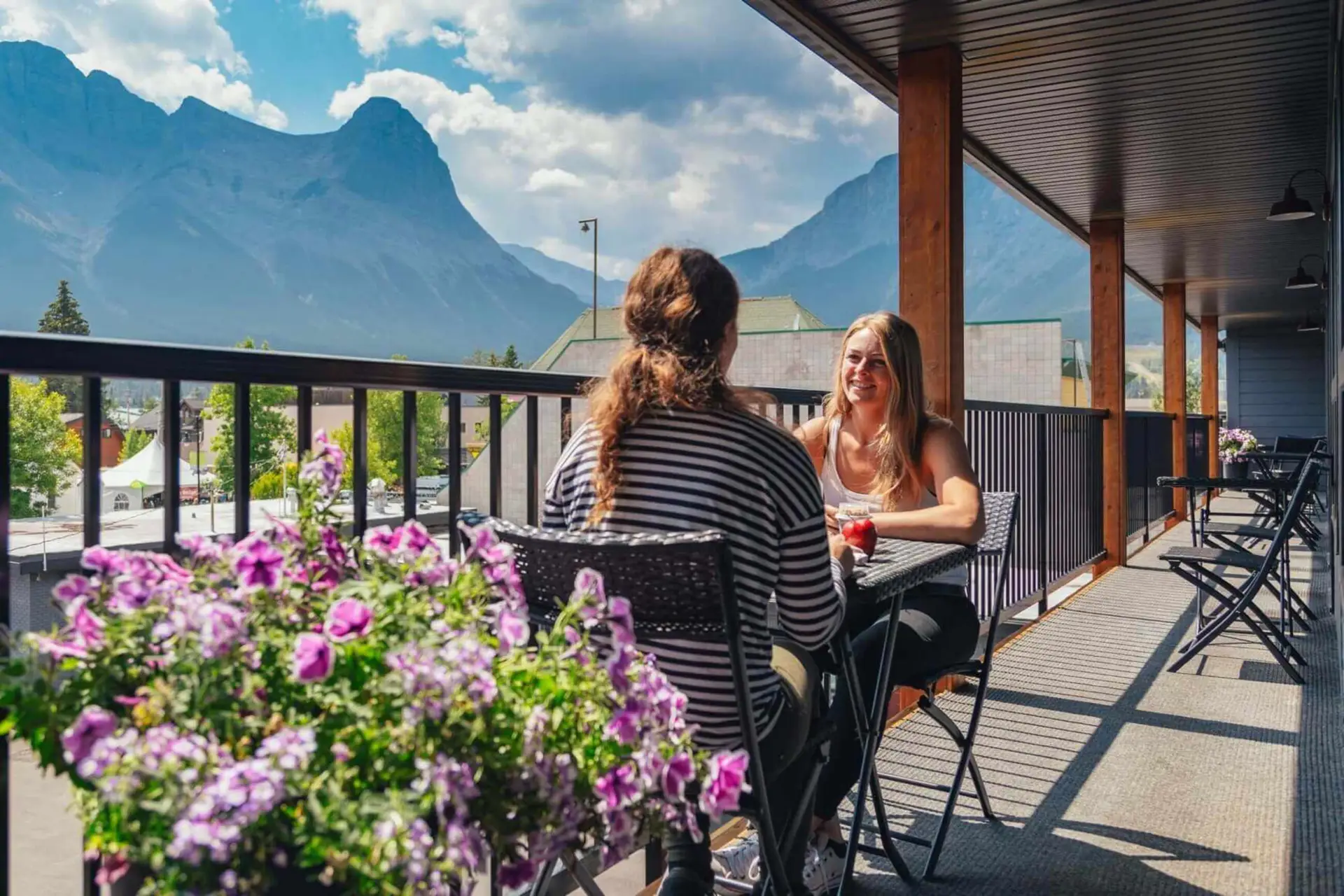 Two women enjoying drinks on a balcony with mountain views