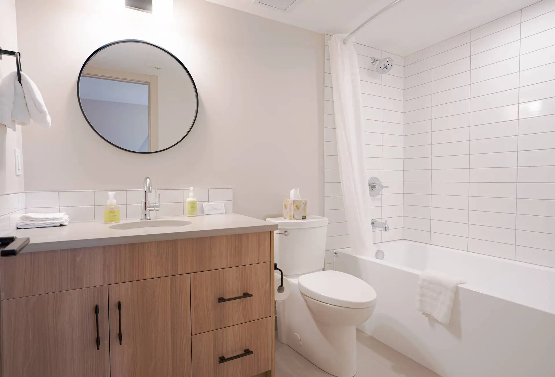 Modern bathroom with white tiles, wooden cabinet, white toilet, and bathtub