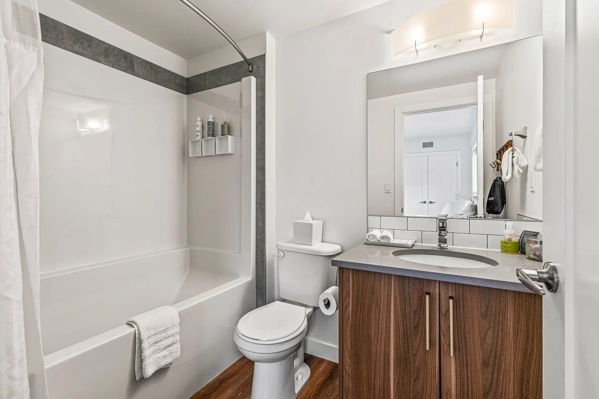 Modern bathroom with white bathtub, toilet, sink, wooden cabinets, mirror, and shower