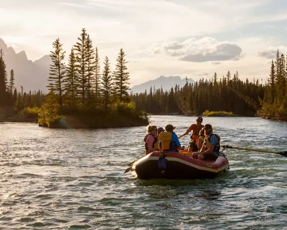 Rafting tour in Canmore with people paddling down a scenic river surrounded by trees and mountains.