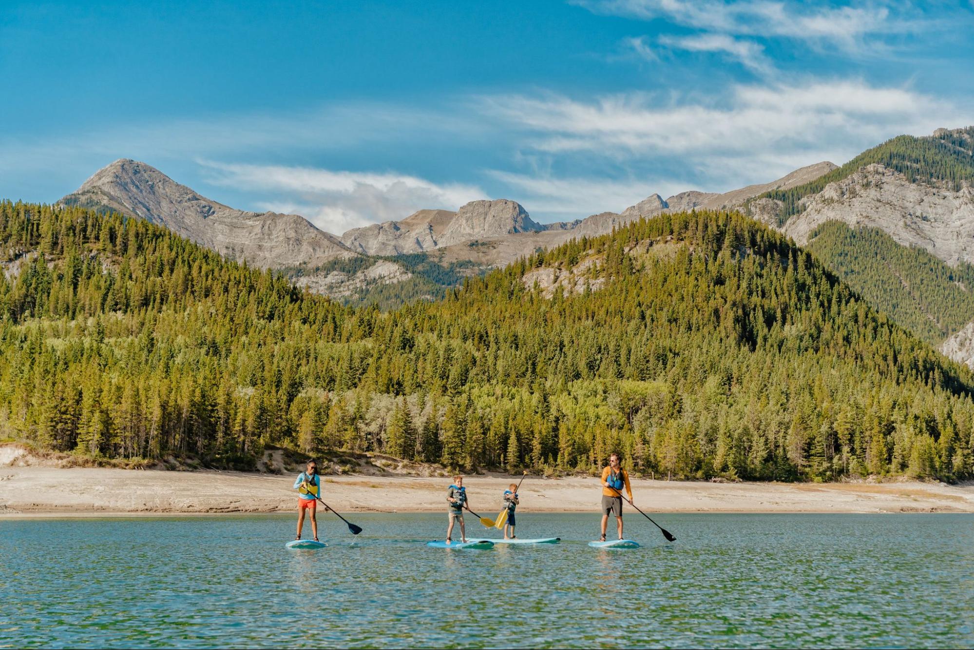 Family paddleboarding on a serene lake with mountains and forest backdrop