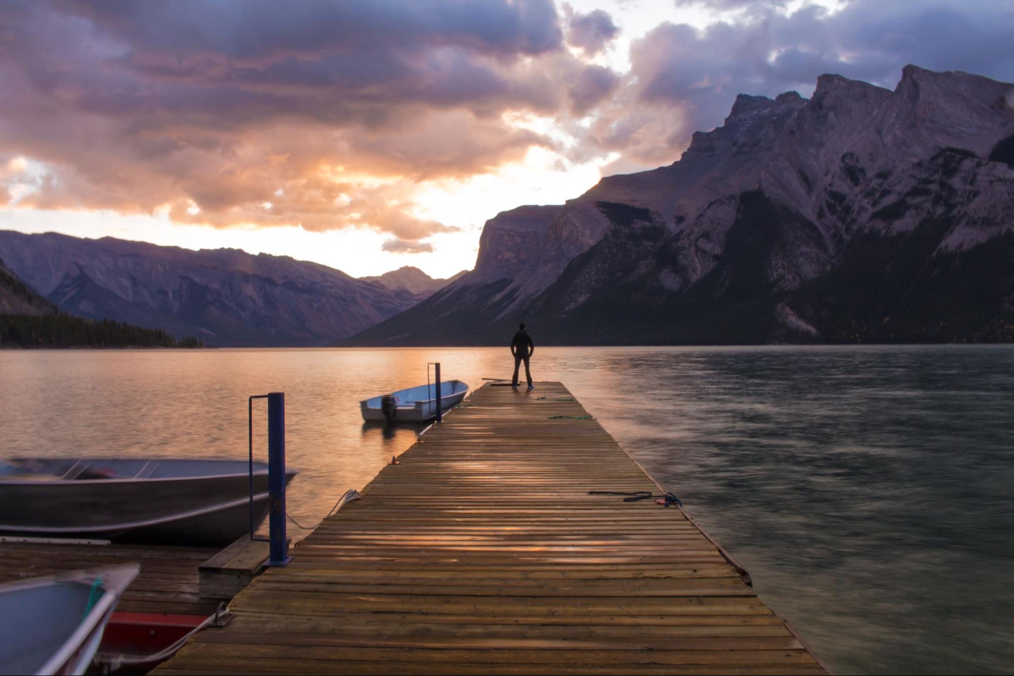Wooden dock on a lake near Banff with mountains and a person at sunset